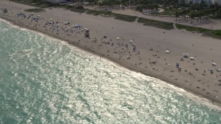 AX0021_056E - 5K aerial stock footage tilt down to people enjoying the beach by condos in South Beach, Florida