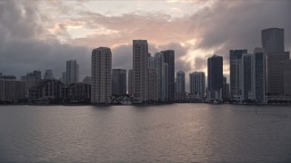 AX0022_061E - 5K aerial stock footage of Downtown Miami coastal skyline at sunset, approach Miami River, Florida