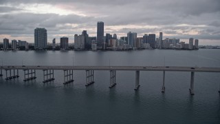 AX0022_076E - 5K aerial stock footage tilt to reveal and fly over Rickenbacker Causeway to approach Downtown Miami at sunset, Florida