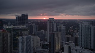 AX0022_088E - 5K aerial stock footage of the setting sun low on the horizon beyond Downtown Miami skyscrapers, Florida