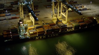 AX0023_062E - 5K aerial stock footage of two cranes loading a cargo ship at night at the Port of Miami, Florida