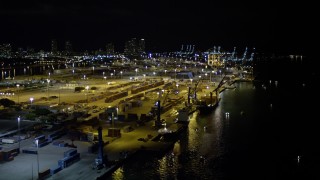 AX0023_152 - 5K aerial stock footage of passing cargo ships docked beneath cranes at the Port of Miami at night, Florida
