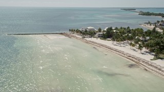 AX0025_130E - 5K aerial stock footage of flying by coastal homes, approach and orbit end of beach, Islamorada, Florida