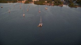 AX0028_034 - 5K aerial stock footage of approaching a catamaran, sailboats at sunset, Key Largo, Florida