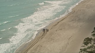 AX0033_028E - 5K aerial stock footage of orbiting horseback riders on the beach by blue ocean waters, Florida