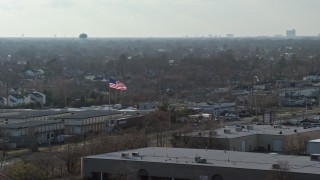 AX0065_0001 - 5K aerial stock footage of an American flag flying over warehouse buildings in Farmingdale, Long Island, New York