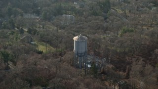 AX0065_0018E - 5K stock footage aerial video fly over leafless trees to approach a water tower in Brookville, Long Island, New York, winter