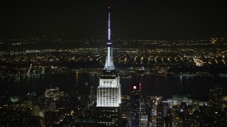 AX0065_0321E - 5K aerial stock footage of orbiting the top of the Empire State Building in Midtown Manhattan, New York City, winter, night
