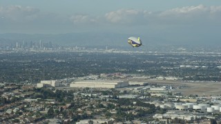 AX0160_061 - 7.6K aerial stock footage of the Goodyear Blimp approaching the airport, Downtown LA skyline in background, Long Beach, California