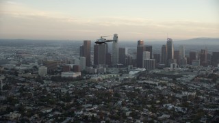 AX0162_092 - 7.6K stock footage aerial video tracking an LAPD helicopter flying by the skyline of Downtown Los Angeles, California at twilight
