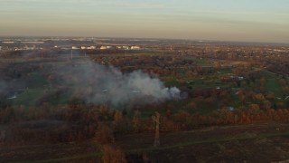 AX0163_0004 - 4K aerial stock footage of a fire in the trees at a golf course at sunset in Lockport, Illinois