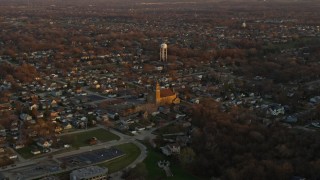 AX0163_0006 - 4K aerial stock footage of passing suburban homes and church near water tower at sunset in Lemont, Illinois