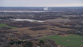 AX0166_0060 - 4K aerial stock footage of smoke rising beyond a rural neighborhood and fields in Muskego, Wisconsin