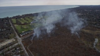 AX0167_0065 - 4K aerial stock footage of smoke rising from a golf course and nature preserve in Glencoe, Illinois