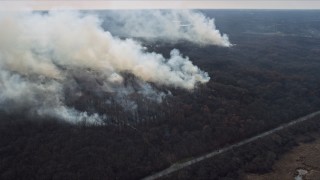 AX0168_0022 - 4K aerial stock footage of approaching plumes of smoke rising from fires in the forest, Willow Springs, Illinois