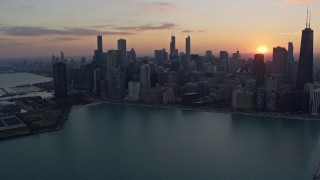 AX0170_0022 - 4K aerial stock footage of flying by the downtown skyline with setting sun in the distance, Downtown Chicago, Illinois