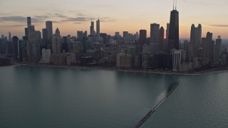 AX0170_0031 - 4K stock footage aerial video tilt from the lake to reveal waterfront skyscrapers and distant sunset, Downtown Chicago, Illinois