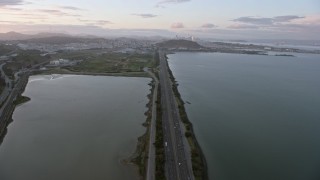 AX0174_0071 - 6K aerial stock footage tilt from Bayshore Fwy to reveal the distant San Francisco skyline at sunset, California