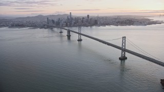 AX0174_0086 - 6K aerial stock footage panning across the Bay Bridge to reveal the Downtown San Francisco skyline at sunset, California