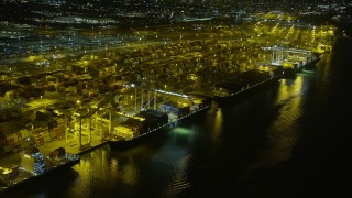 AX0174_0200 - 6K stock footage aerial video passing by cargo ships docked at the Port of Oakland at night, California