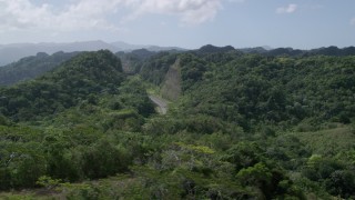 AX101_078 - 4.8K aerial stock footage of Light traffic cutting through lush green mountains, Karst Forest, Puerto Rico 