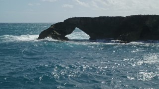 AX101_168E - 4.8K aerial stock footage of an arched rock formation in crystal blue waters, Arecibo, Puerto Rico