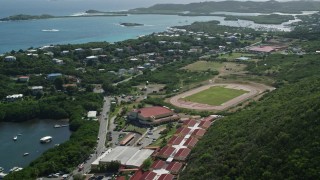 AX102_244 - 4.8K stock footage aerial video of a High school track field near blue coastal waters, East End, St Thomas
