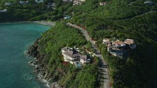 AX103_041E - 4.8K aerial stock footage of a coastal road and mansions with turquoise blue water on either side, Cruz Bay, St John