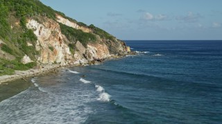 AX103_048E - 4.8K aerial stock footage flying low by a Caribbean beach and sapphire blue waters cliffside, Reef Bay, St John