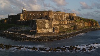 AX104_030 - 4.8K aerial stock footage of Fort San Felipe del Morro along calm ocean waters, Old San Juan, sunset
