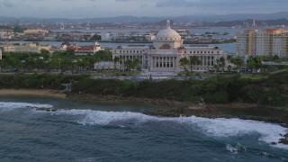 AX104_051 - 4.8K aerial stock footage of the San Juan Capitol Building along the ocean, Old San Juan, Puerto Rico, sunset