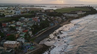 AX104_078E - 4.8K aerial stock footage of passing oceanfront homes near a cemetery on the way to fort and lighthouse, Old San Juan, Puerto Rico, sunset