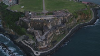 AX104_090 - 4.8K aerial stock footage of Fort San Felipe del Morro along Caribbean blue ocean waters, Old San Juan, twilight