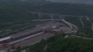 AX108_008E - 4K aerial stock footage approaching a factory and bridge surrounded by trees, East Pittsburgh, Pennsylvania