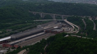 AX108_009 - 4K aerial stock footage approaching a factory and bridge among trees, East Pittsburgh, Pennsylvania
