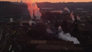 AX108_027 - 4K aerial stock footage of smoke rising from the U.S. Steel Mon Valley Works, Braddock, Pennsylvania, sunset