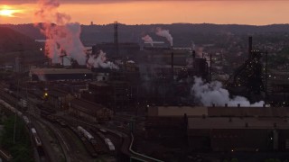AX108_027E - 4K aerial stock footage of smoke rising from the U.S. Steel Mon Valley Works, Braddock, Pennsylvania, sunset