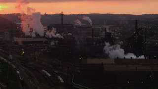 AX108_028 - 4K aerial stock footage of smoke rising from the U.S. Steel Mon Valley Works, Braddock, Pennsylvania, sunset