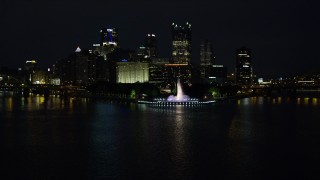 AX108_217E - 4K aerial stock footage descend to river, fly over Point State Park toward skyscrapers, Downtown Pittsburgh, night
