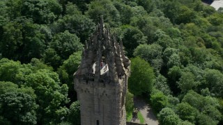 AX109_052E - 5.5K aerial stock footage of orbiting top of iconic Wallace Monument surrounded in trees, Stirling, Scotland