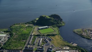 AX110_140E - 5.5K aerial stock footage of Dumbarton Castle and soccer stadium beside the water, Scotland
