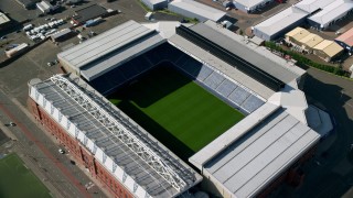 AX110_201 - 5.5K stock footage aerial video approach Ibrox Stadium, tilt to bird's eye of soccer field, Glasgow, Scotland