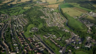 AX111_004E - 5.5K aerial stock footage fly over village homes and farm fields by a river, Bonnybridge, Scotland