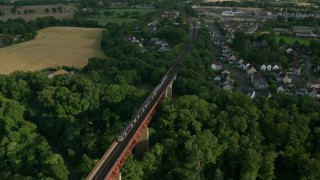 AX111_083 - 5.5K stock footage aerial video of flying over a commuter train moving between trees on Forth Bridge, Scotland