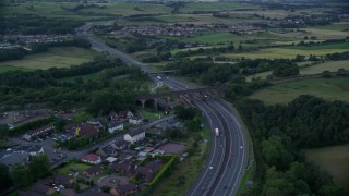 AX112_160 - 5.5K aerial stock footage of orbiting M80 Highway near rural homes, Cumbernauld, Scotland at twilight