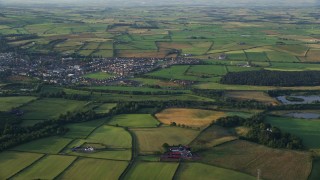 AX113_028E - 5.5K aerial stock footage video of a village surrounded by farm fields, Tarbolton, Scotland at sunrise