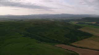 AX113_052 - 5.5K aerial stock footage of flying by hilly moorland, reveal farms, Maybole, Scotland