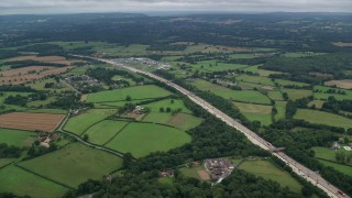 AX114_363E - 5.5K aerial stock footage of a shopping center beside farm fields and freeway, Cobham, England