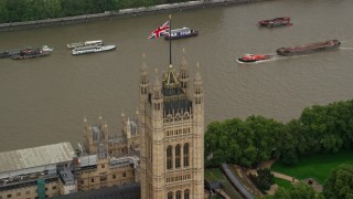 AX115_101 - 5.5K aerial stock footage of orbiting British Flag atop Parliament along River Thames, London England