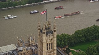 AX115_101E - 5.5K aerial stock footage of orbiting British Flag atop Parliament along River Thames, London England